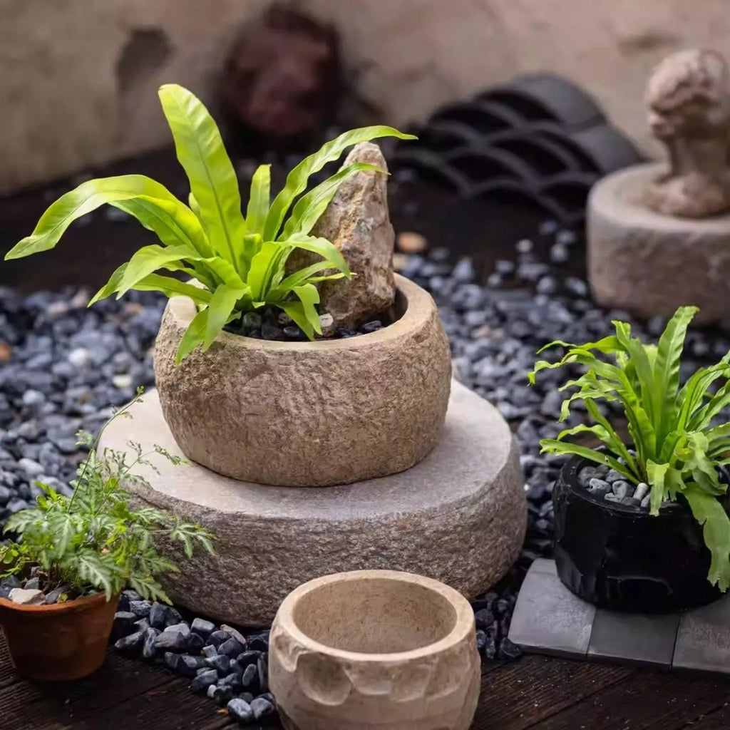 Sand cement planters with a fern and dark pebbles, beside a small black planter and a round stone base