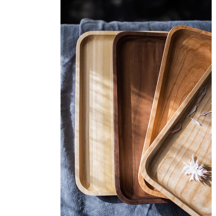 Rectangle serving trays in boxwood, walnut and cherry overlapped in a row on dark gray linen