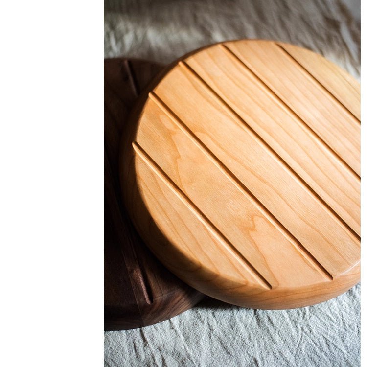 Round pale wood tray with a grooved, slatted surface resting on a walnut tray over gray linen