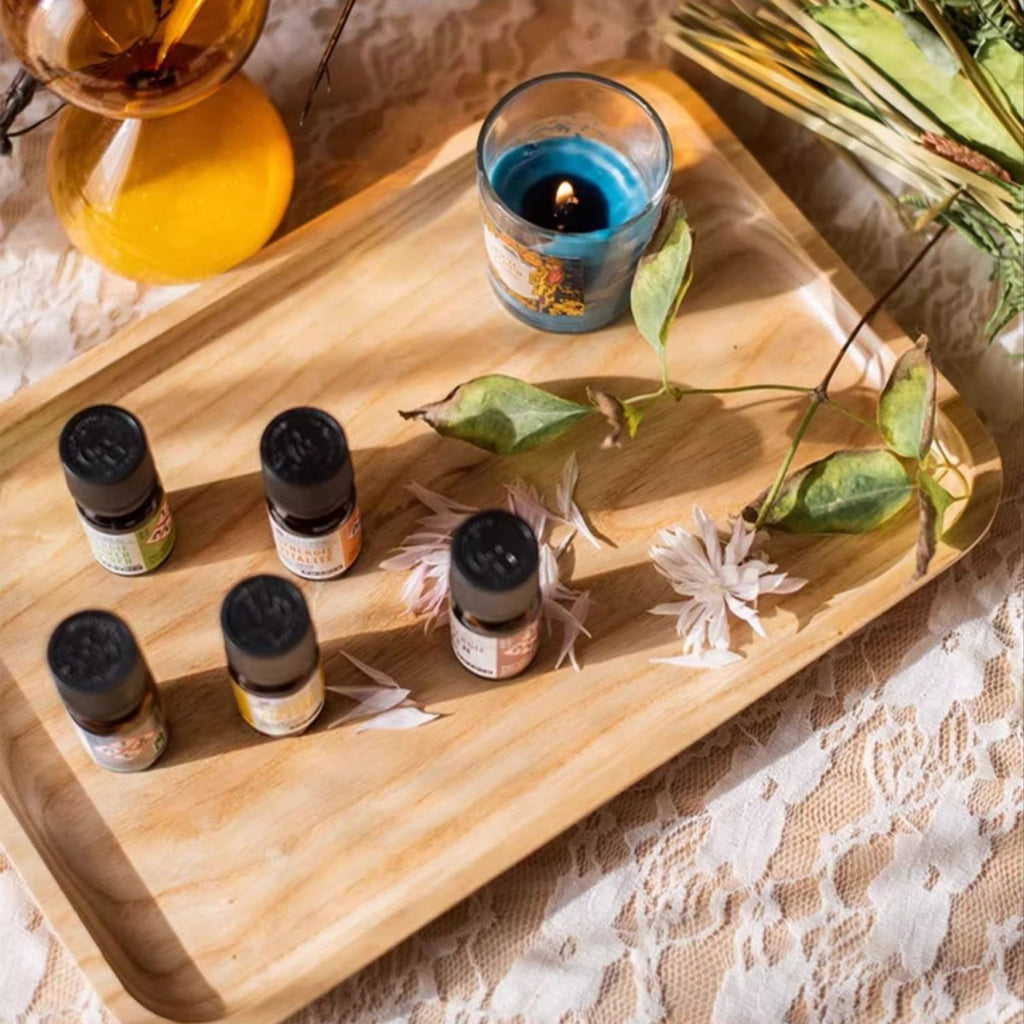 Rectangle cherry wood serving tray with small bottles, a blue candle and pressed flowers on white lace