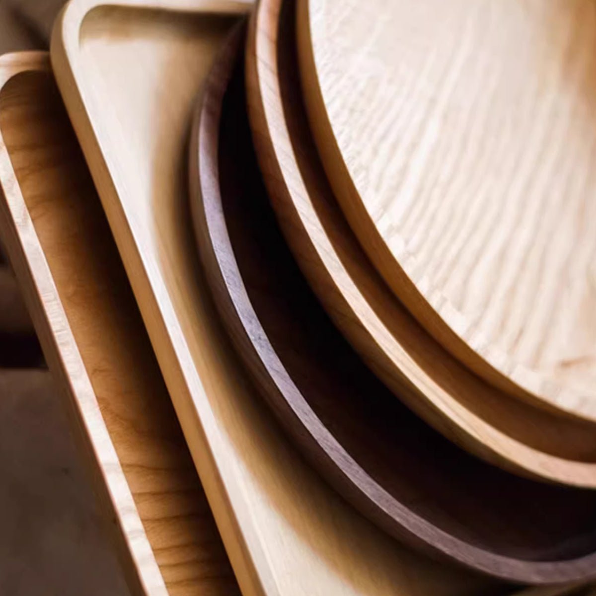 Close view of round and rectangle wood serving trays in ash, cherry and walnut, showing the rounded rims