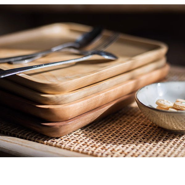 Stack of rectangle ash wood serving trays on a woven rattan mat with forks and a small bowl of cookies