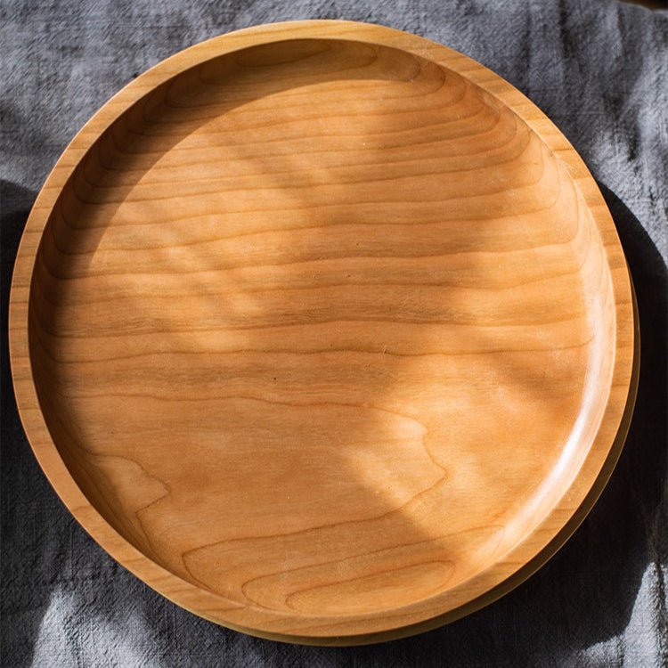 Round cherry wood serving tray from above on gray linen, showing the flowing grain and low rounded rim