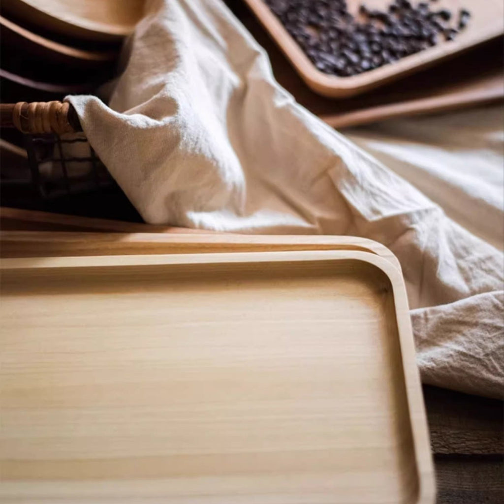 Rectangle boxwood serving tray in pale wood on cream linen, with more trays and coffee beans behind it