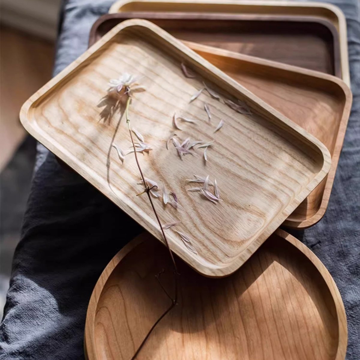 Rectangle ash wood serving tray with dried petals, stacked on walnut and cherry trays above a round tray