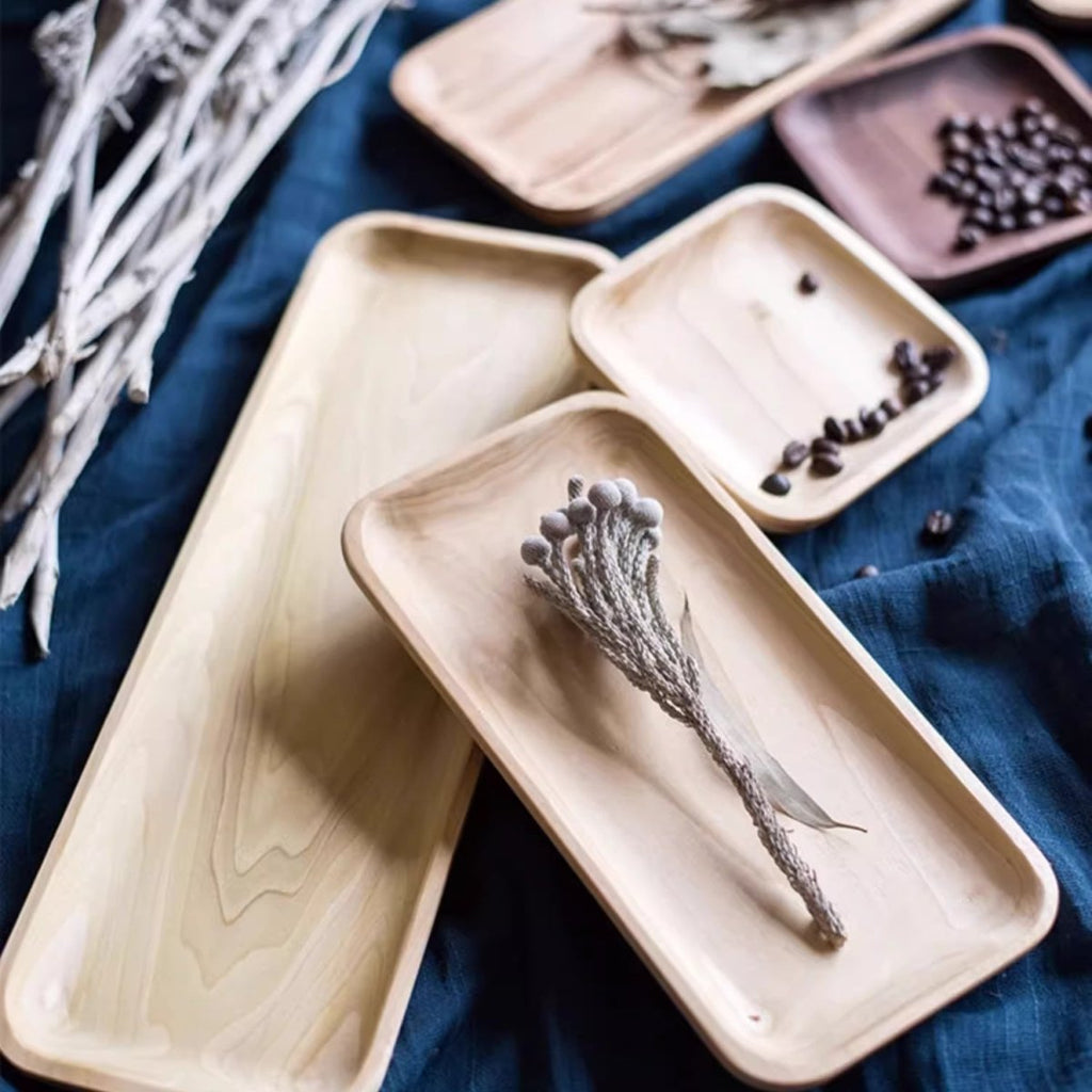 Long boxwood and small ash snack plates on blue linen with dried flowers and a few coffee beans