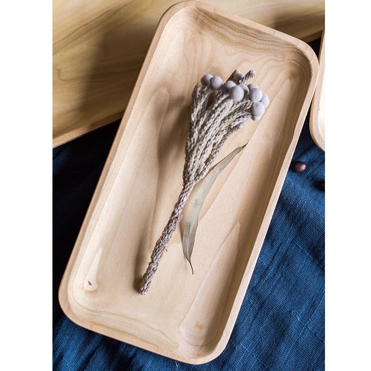 Long boxwood snack plate in pale wood with a sprig of dried grass, set on deep blue linen from above