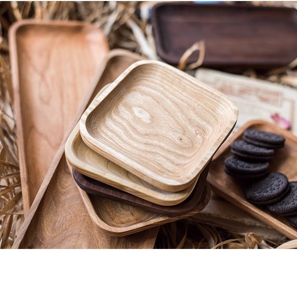 Small square snack plates in ash and walnut stacked on long plates, with cookies on a cherry plate
