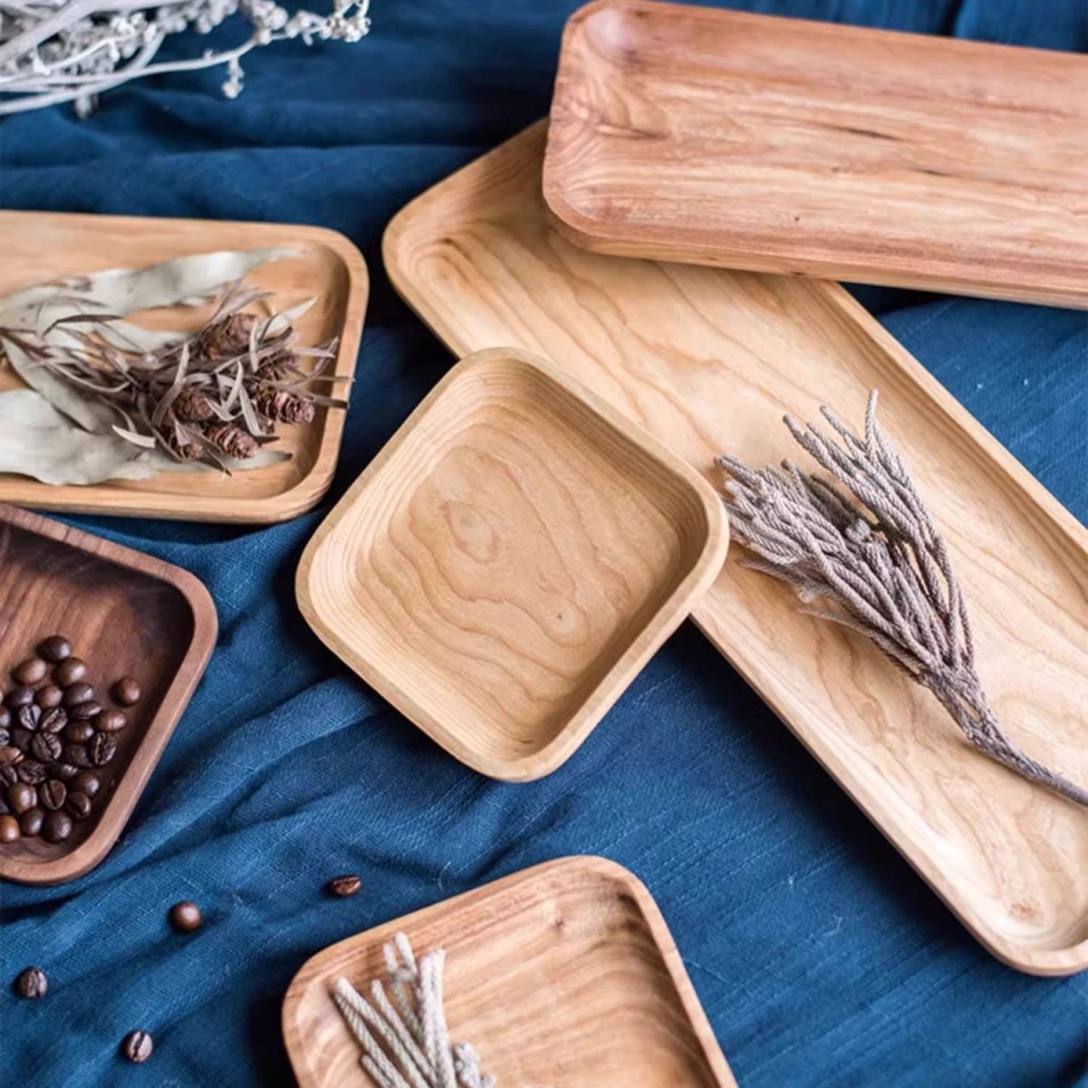 Cherry and walnut snack plates in three lengths on blue linen, holding dried herbs and coffee beans