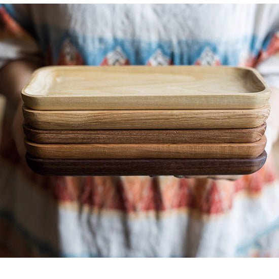 Stack of long wood snack plates in ash, cherry and walnut held at waist height against a print apron