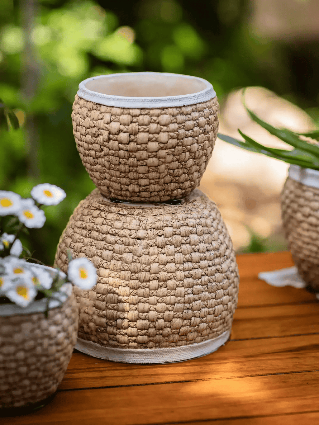 Three woven texture cement planters with ivory rims stacked on a wooden deck outdoors