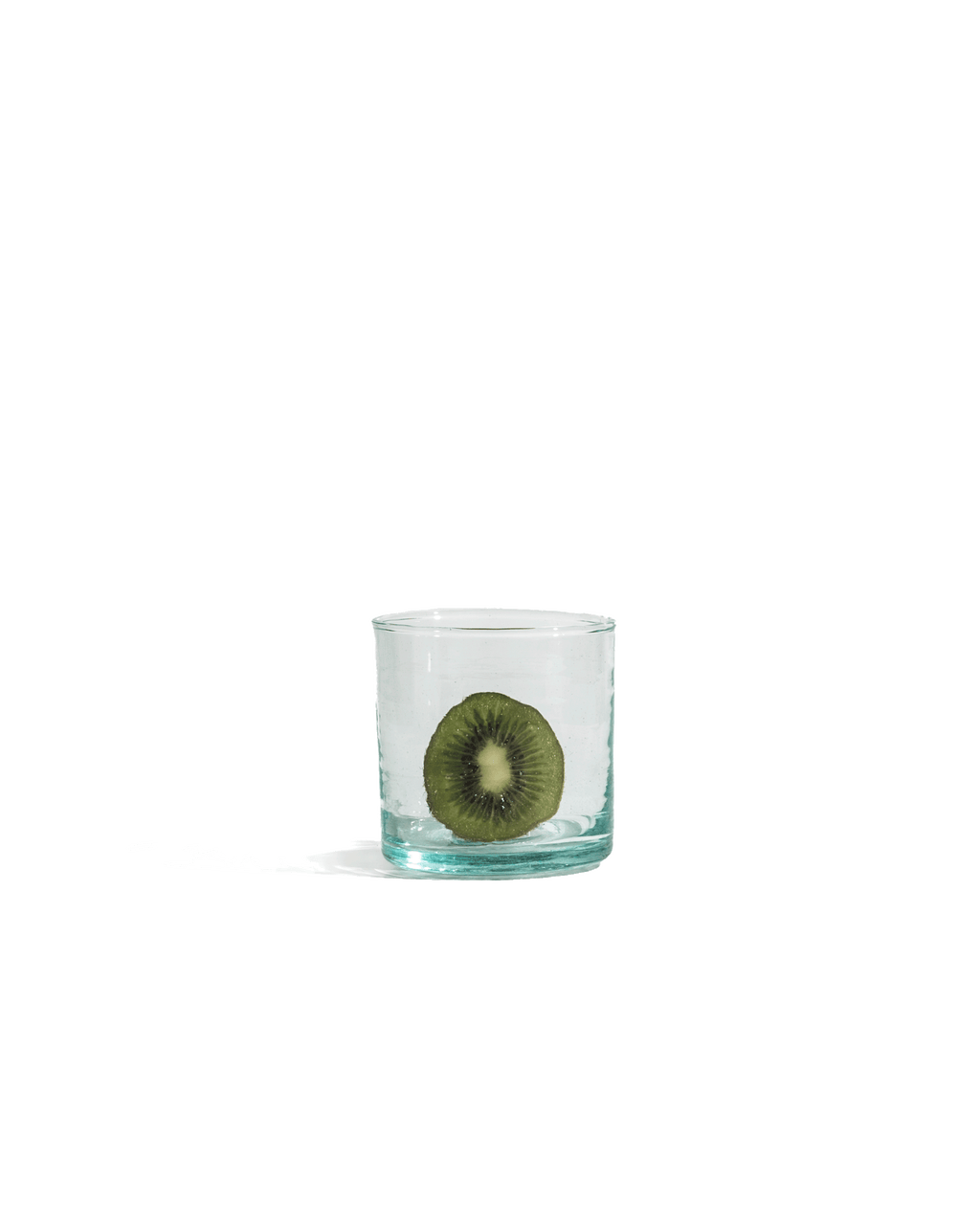 Medium hand-blown recycled glass tumbler holding a halved kiwi, shown on a solid deep green ground