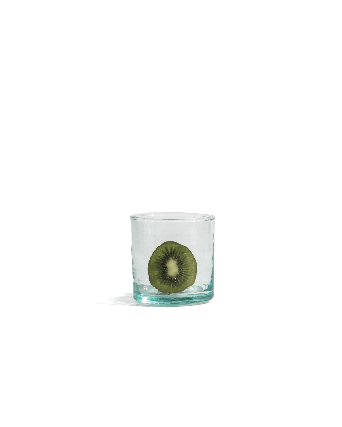 Medium hand-blown recycled glass tumbler holding a halved kiwi, shown on a solid deep green ground