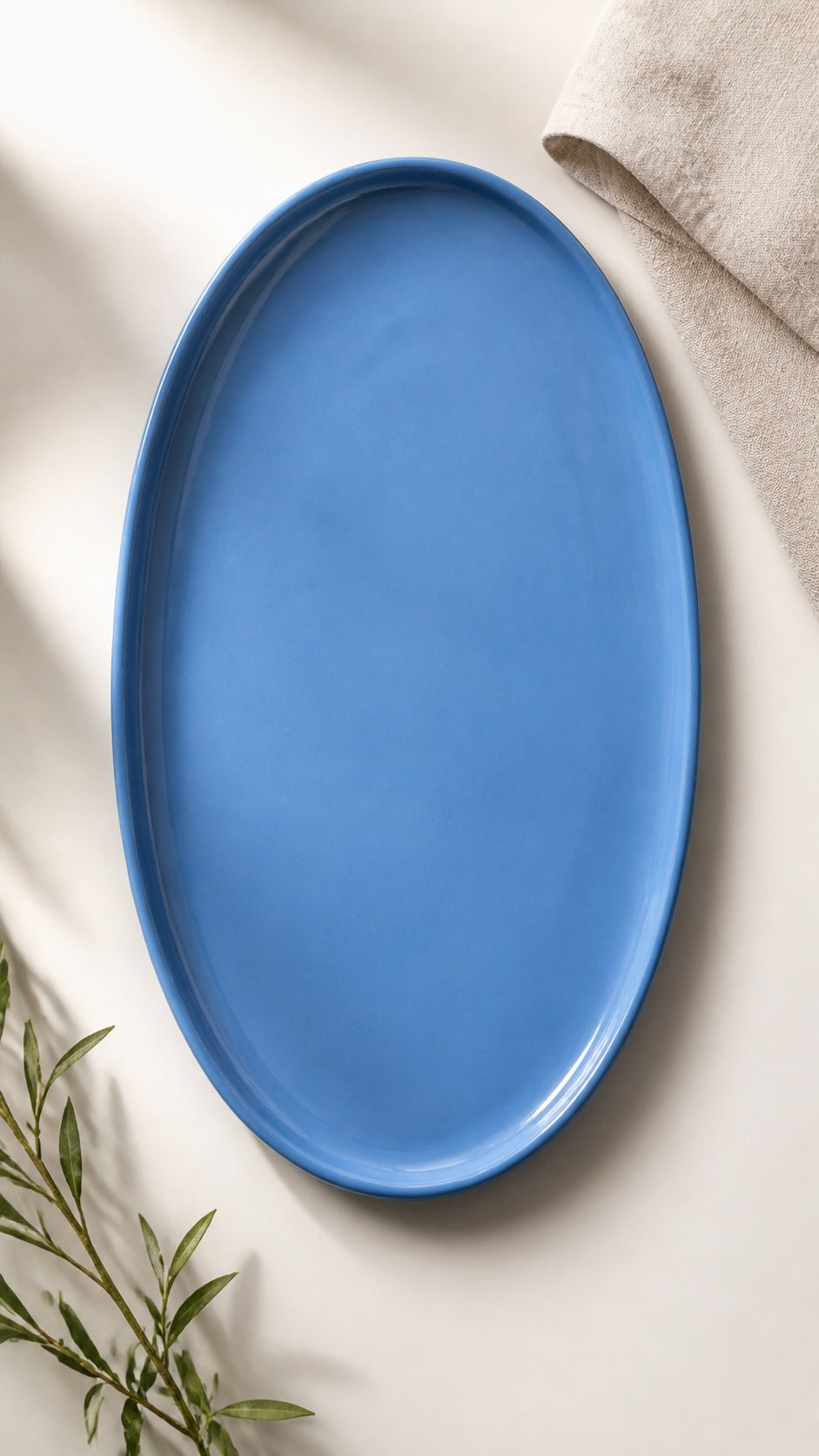 One large blue oval porcelain platter on rumpled linen with a sprig of dried grass at the edge