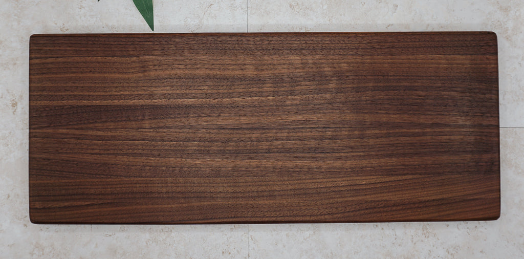 Large dark walnut serving board seen from above on a pale stone surface with green leaves
