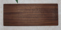 Large dark walnut serving board seen from above on a pale stone surface with green leaves