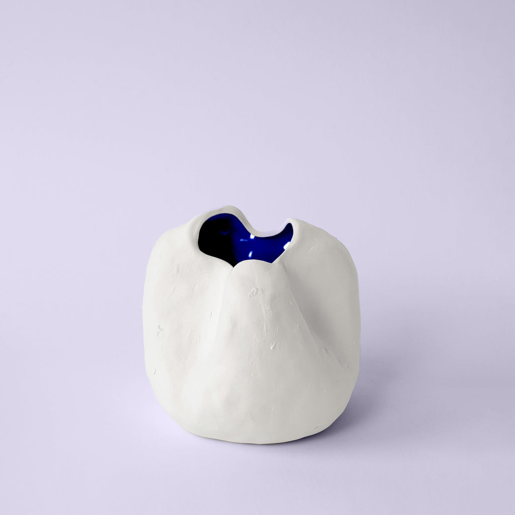 Small rounded white porcelain vase with a pinched rim and cobalt blue interior on a lavender backdrop