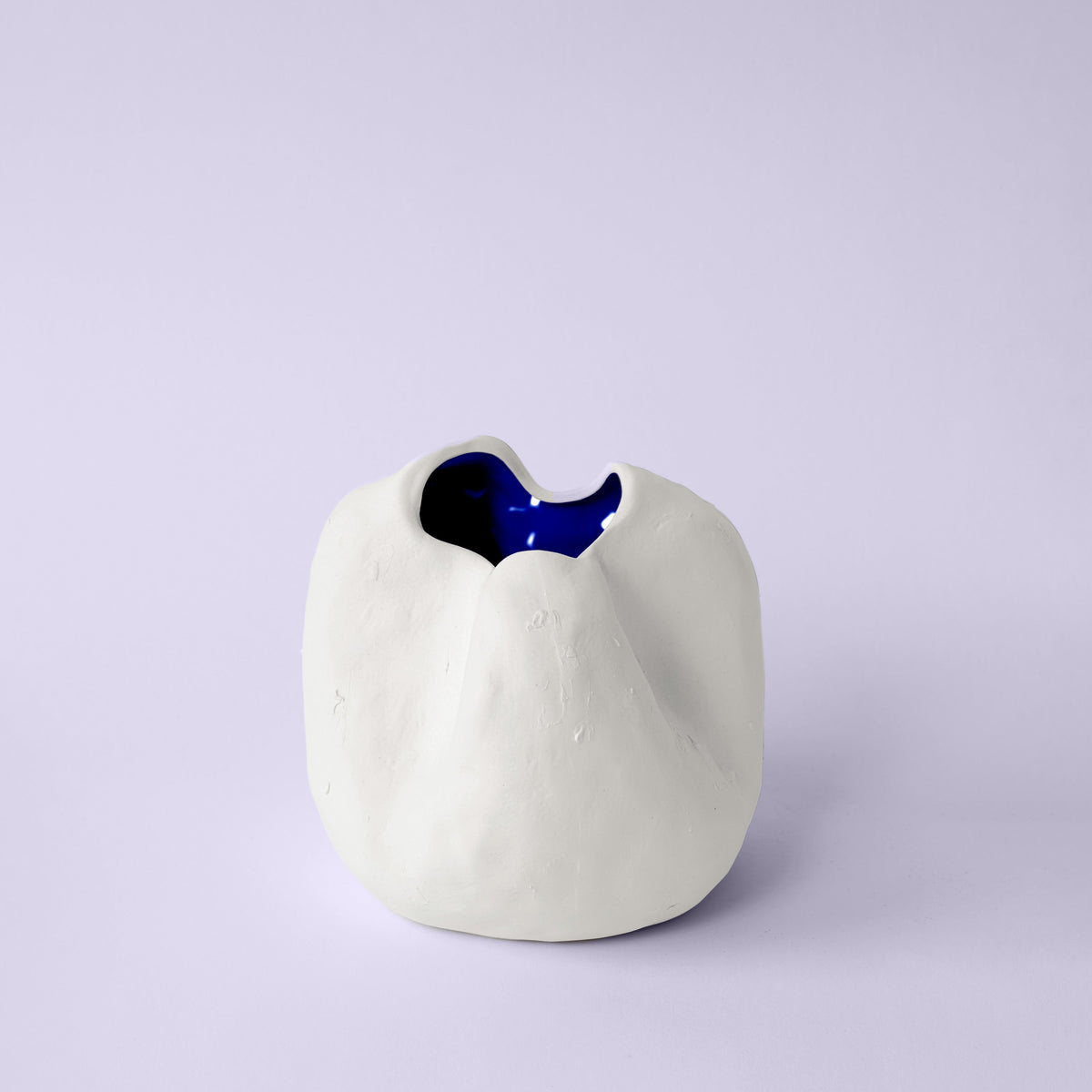 Small rounded white porcelain vase with a pinched rim and cobalt blue interior on a lavender backdrop