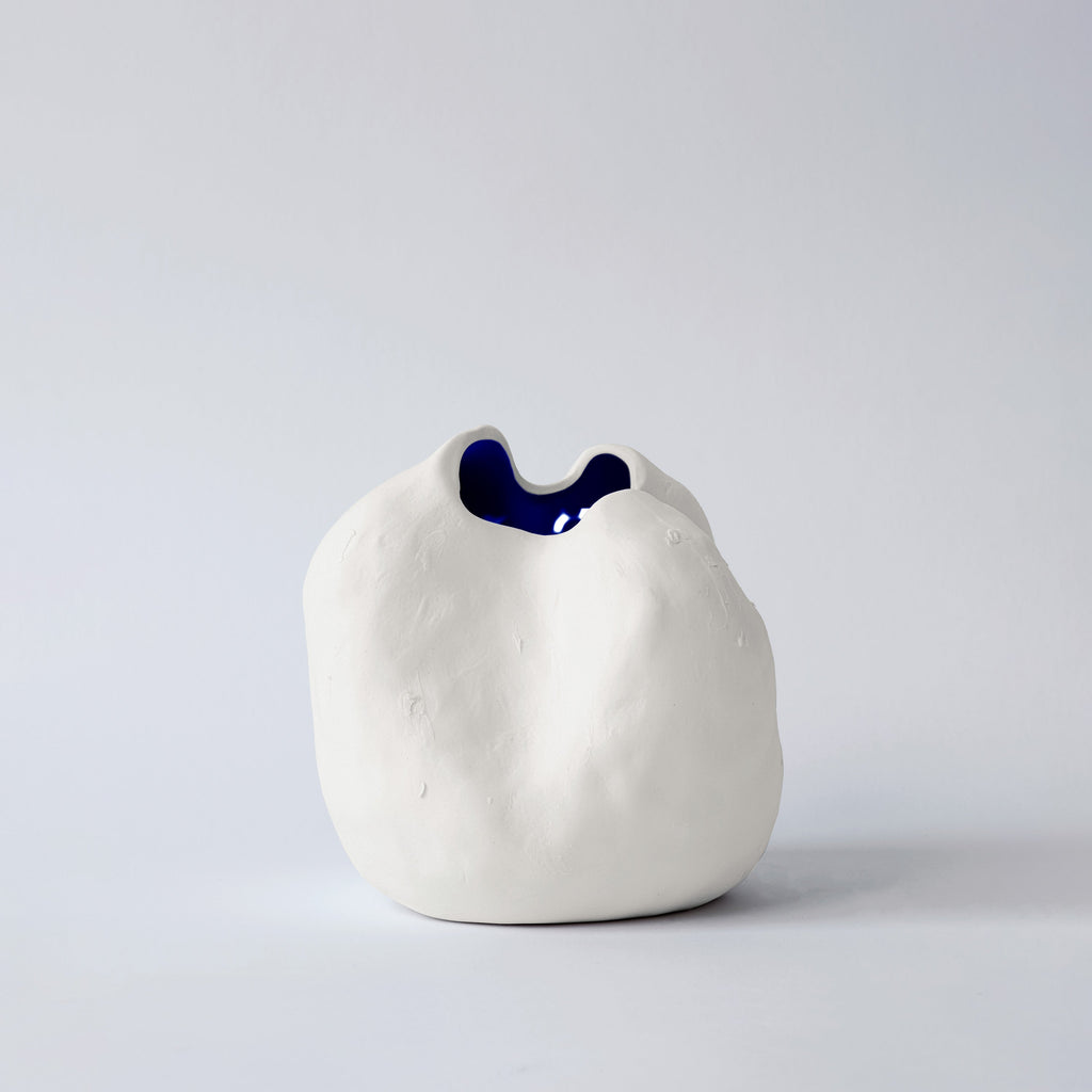 Small white sculpted porcelain vase seen from the front with a glimpse of its glossy cobalt interior