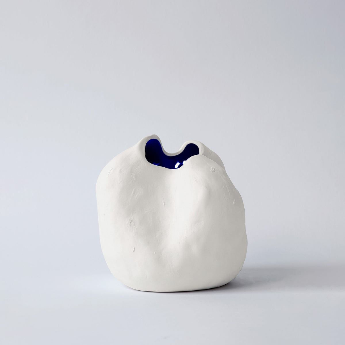 Small white sculpted porcelain vase seen from the front with a glimpse of its glossy cobalt interior
