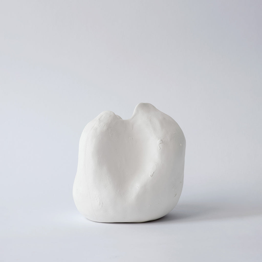 Small rounded white porcelain vase with a dipped, uneven rim shown alone on a pale grey backdrop