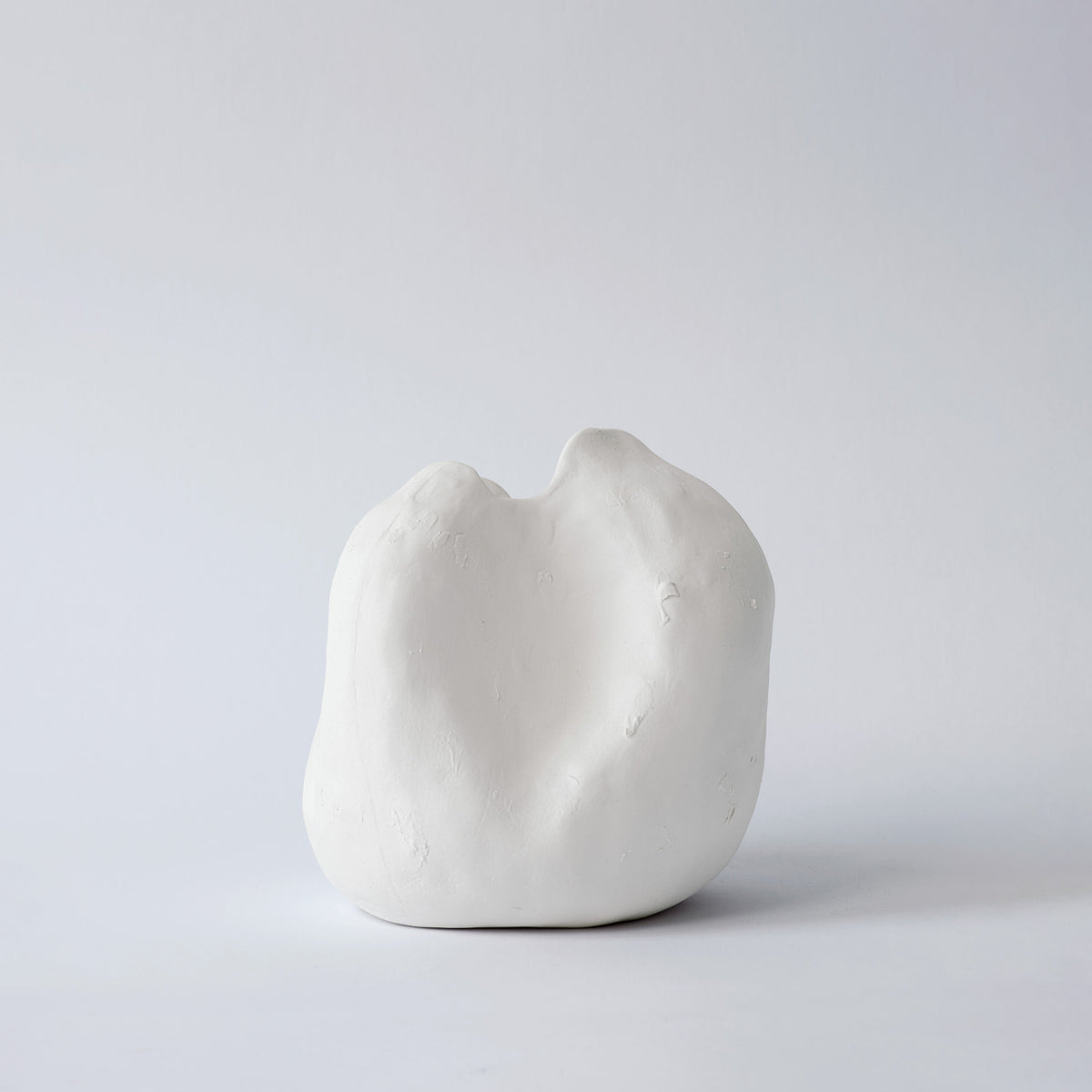 Small rounded white porcelain vase with a dipped, uneven rim shown alone on a pale grey backdrop