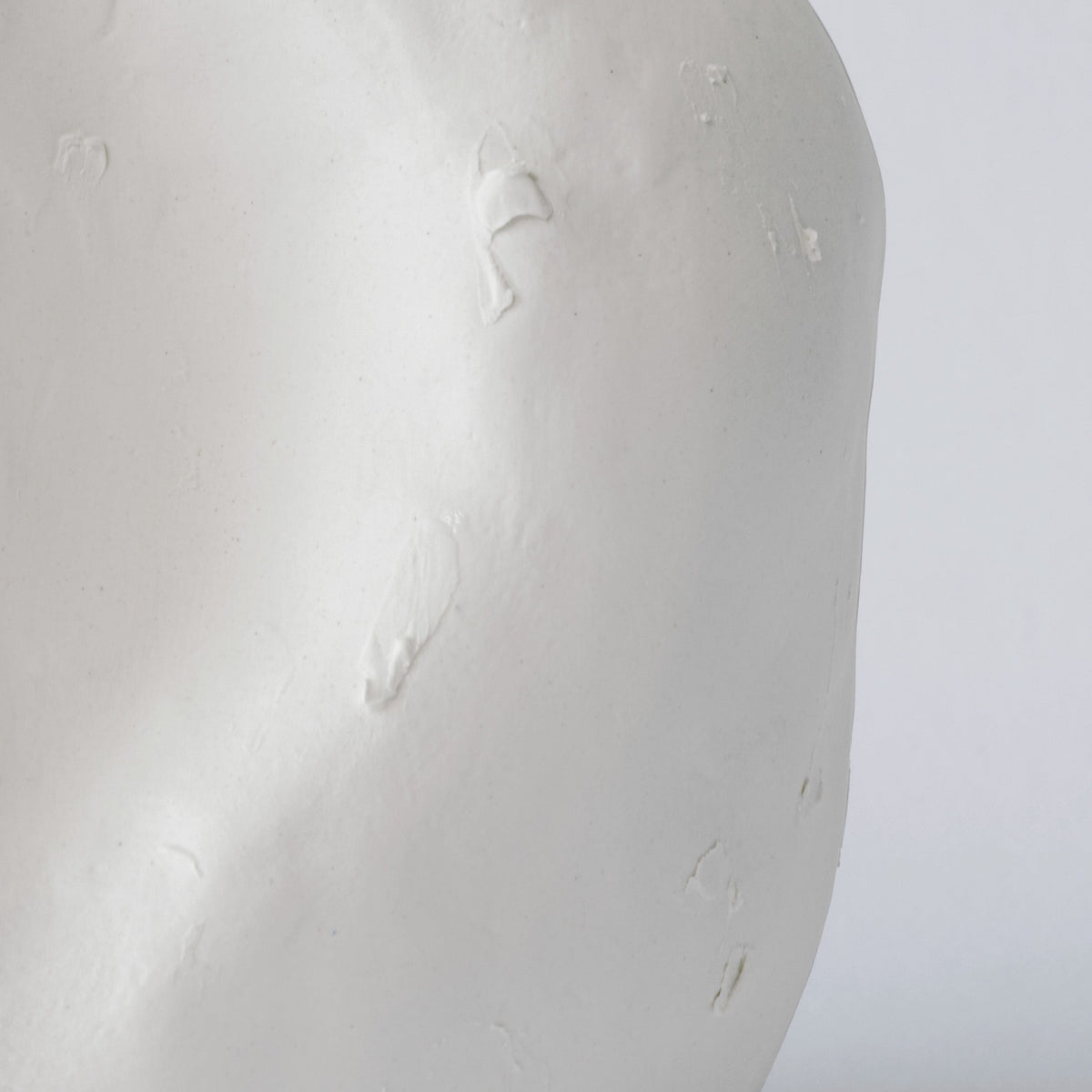 Close detail of the matte white surface of a hand-sculpted porcelain vase showing its soft ridges