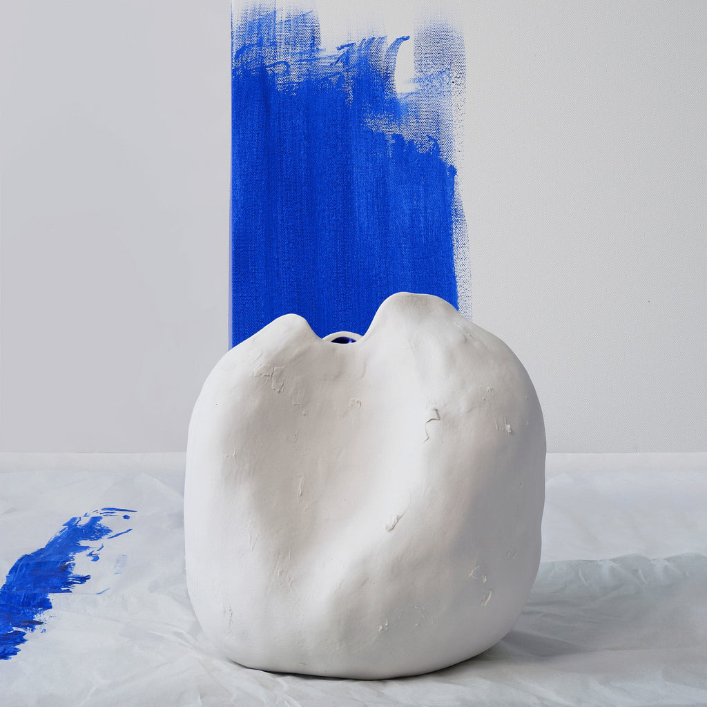 Small sculpted white porcelain vase on a paint-spattered cloth in front of a bold cobalt brushstroke