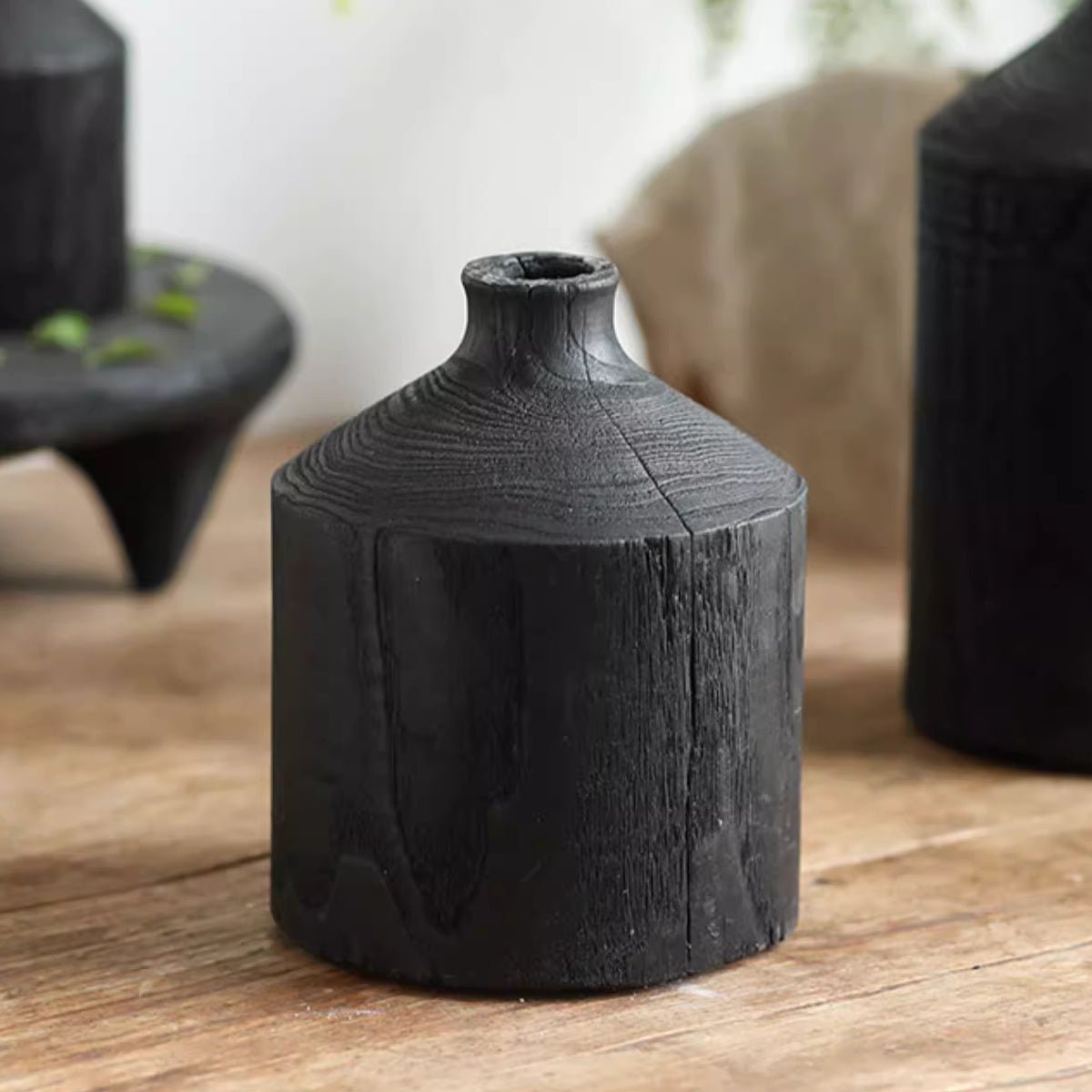 Medium black wood bottle vase on a wood table, with its narrow neck and visible grain and checks