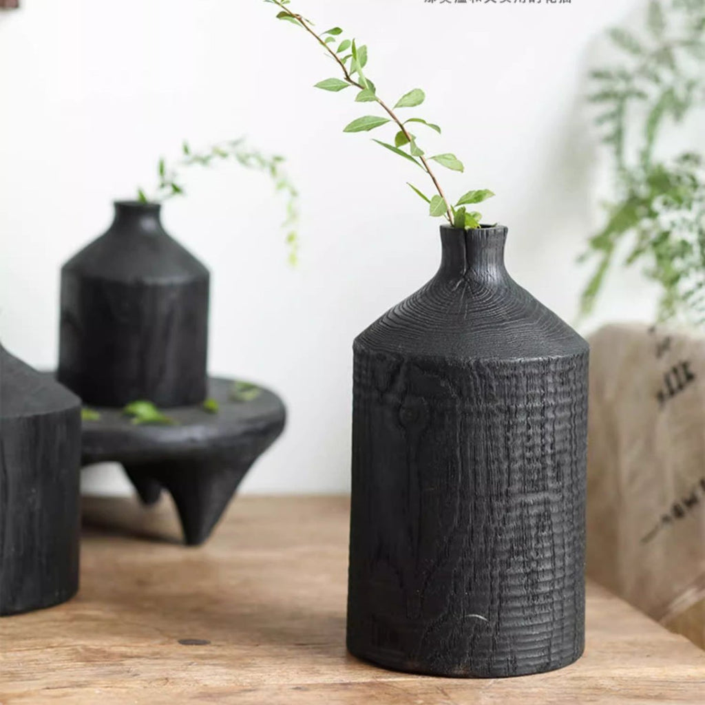 Large black wood bottle vase with a green sprig, its tall body showing vertical grain and texture