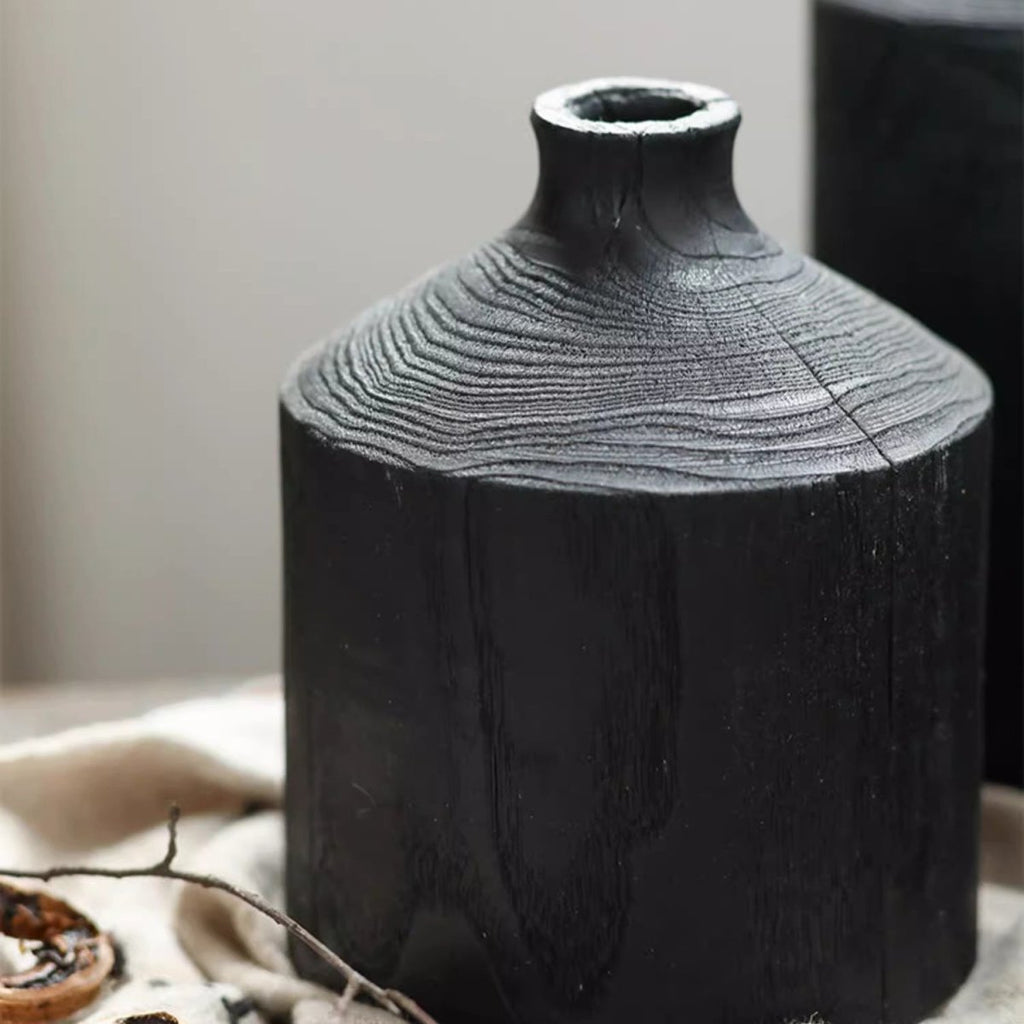 Medium black wood bottle vase on cream linen with a small branch, showing ring grain and the narrow neck