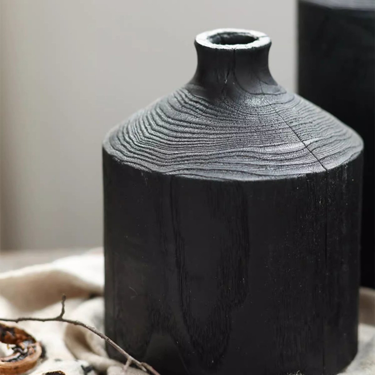 Medium black wood bottle vase on cream linen with a small branch, showing ring grain and the narrow neck