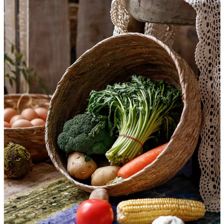 Medium seagrass bowl basket tipped on its side, spilling broccoli, leafy greens and a carrot