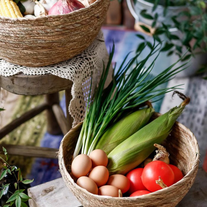 Seagrass bowl basket of eggs, corn and tomatoes on a stool, with another basket stacked above it