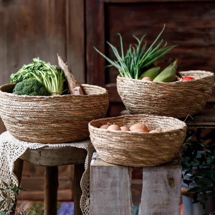 Three seagrass bowl baskets in small, medium and large on wooden crates, filled with eggs and greens