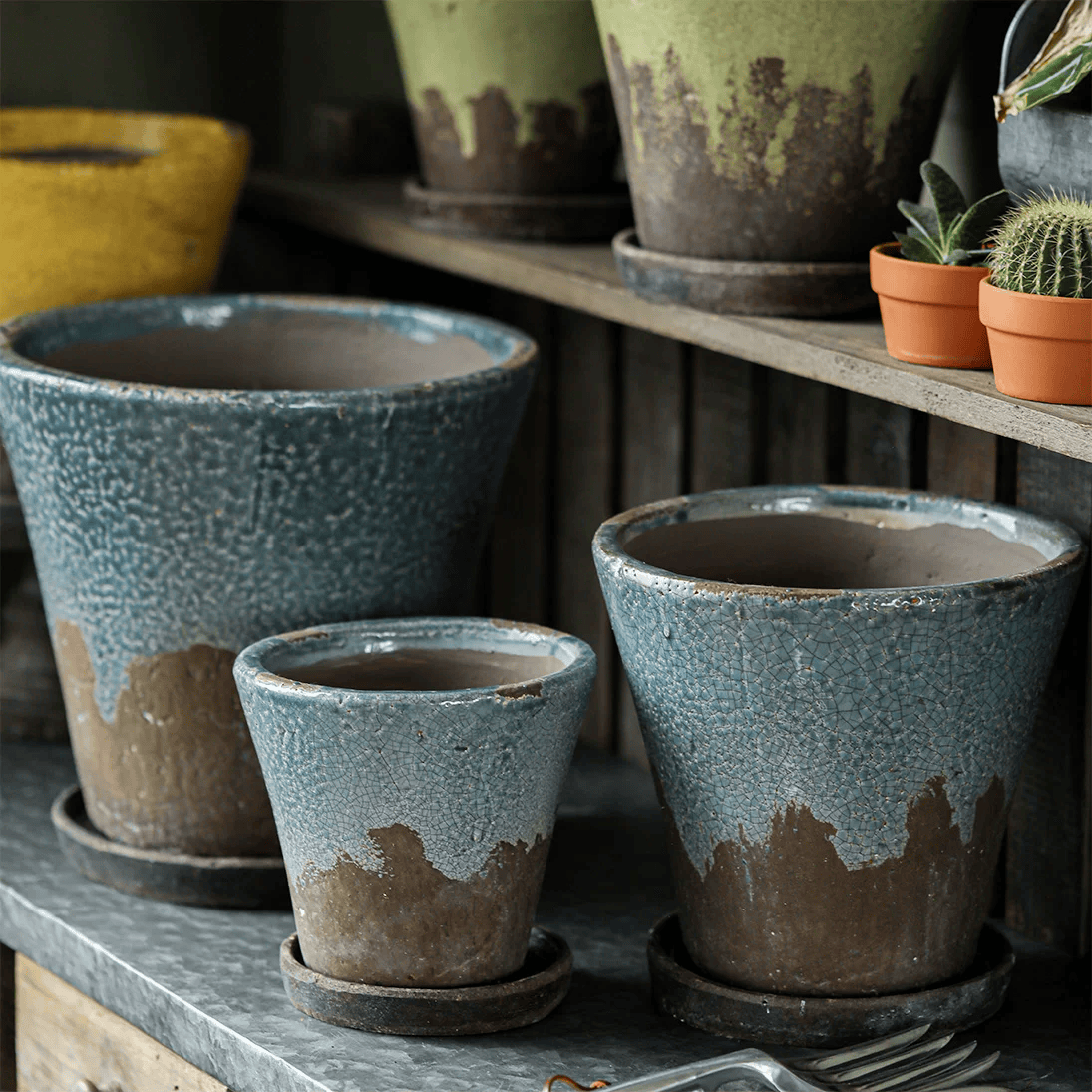 Slate blue crackle glaze ceramic planters with saucers in three sizes on a zinc-topped table