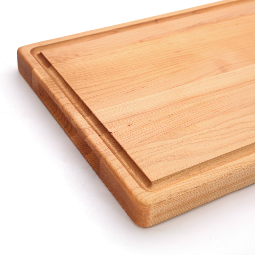 Corner close-up of a thick maple cutting board showing the juice groove and squared edge