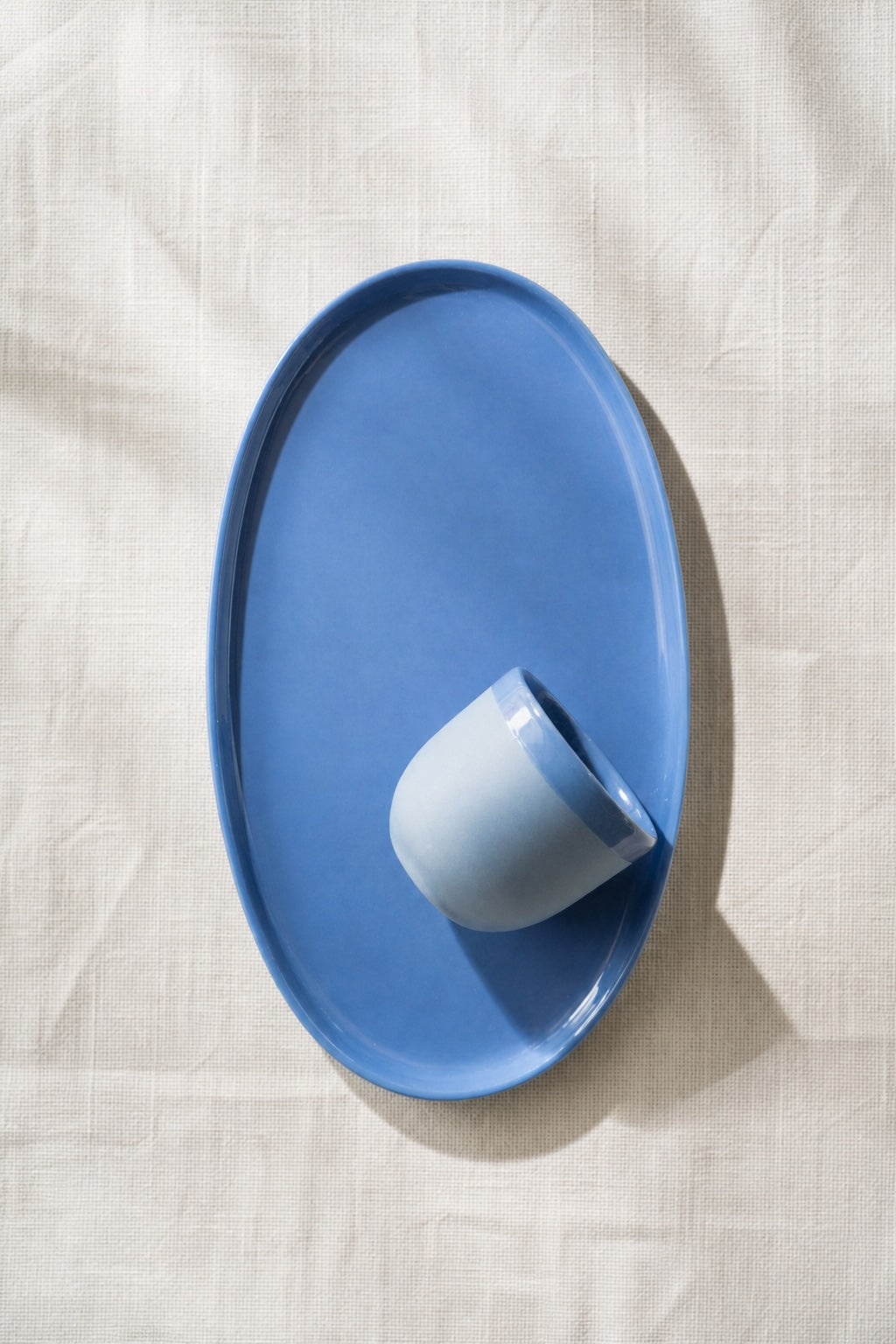Blue oval porcelain platter holding a pale ceramic cup on a soft white linen cloth