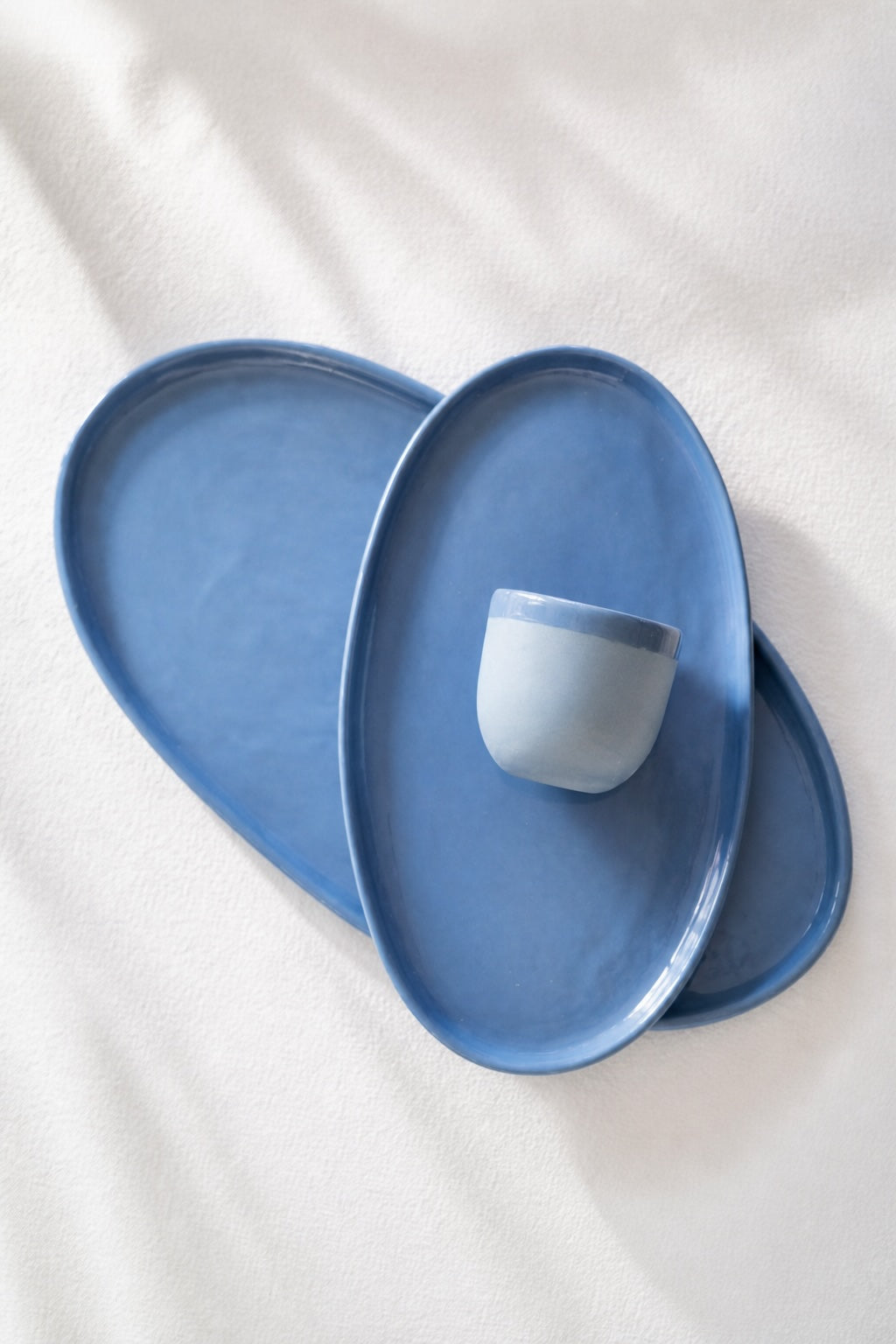 Overlapping blue porcelain platters with a white cup resting on top, shown from above on linen