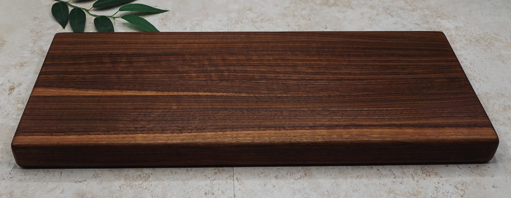 Long walnut board shown straight on to display its striped edge-grain pattern on pale stone