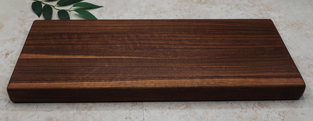Long walnut board shown straight on to display its striped edge-grain pattern on pale stone