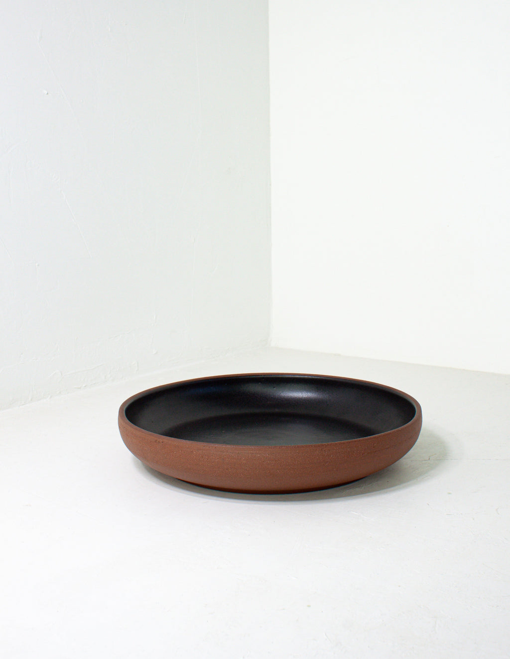 Low coupe serving bowl with a bare terracotta base and black glazed interior on a pale gray ground