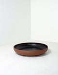 Low coupe serving bowl with a bare terracotta base and black glazed interior on a pale gray ground