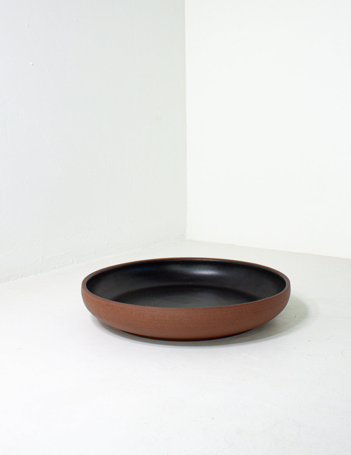 Low coupe serving bowl with a bare terracotta base and black glazed interior on a pale gray ground