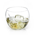 Round recycled glass whiskey tumbler with a dented side holding whiskey and large ice cubes