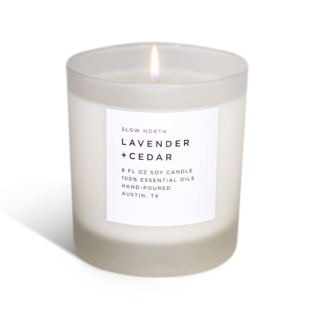 Frosted glass lavender and cedar soy candle with a white label, lit against a plain white background