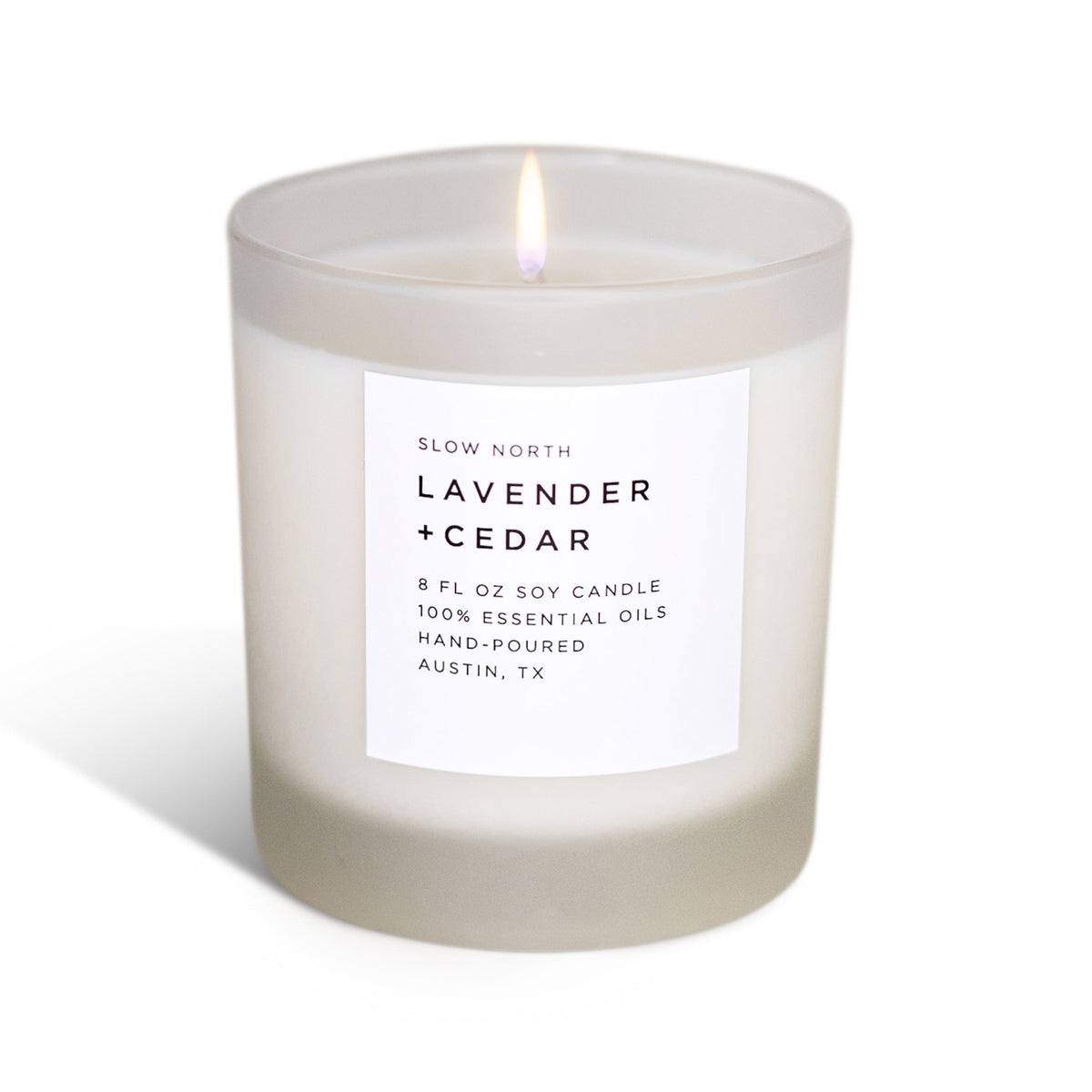 Frosted glass lavender and cedar soy candle with a white label, lit against a plain white background