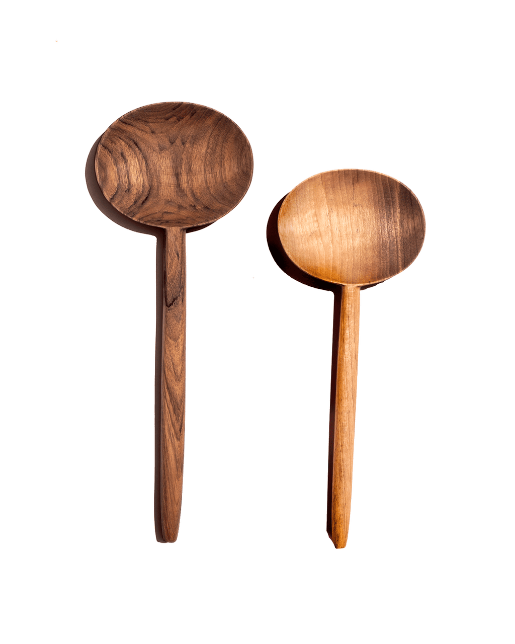 Two carved walnut oval serving spoons, one dark and one honey-toned, laid side by side on a green background