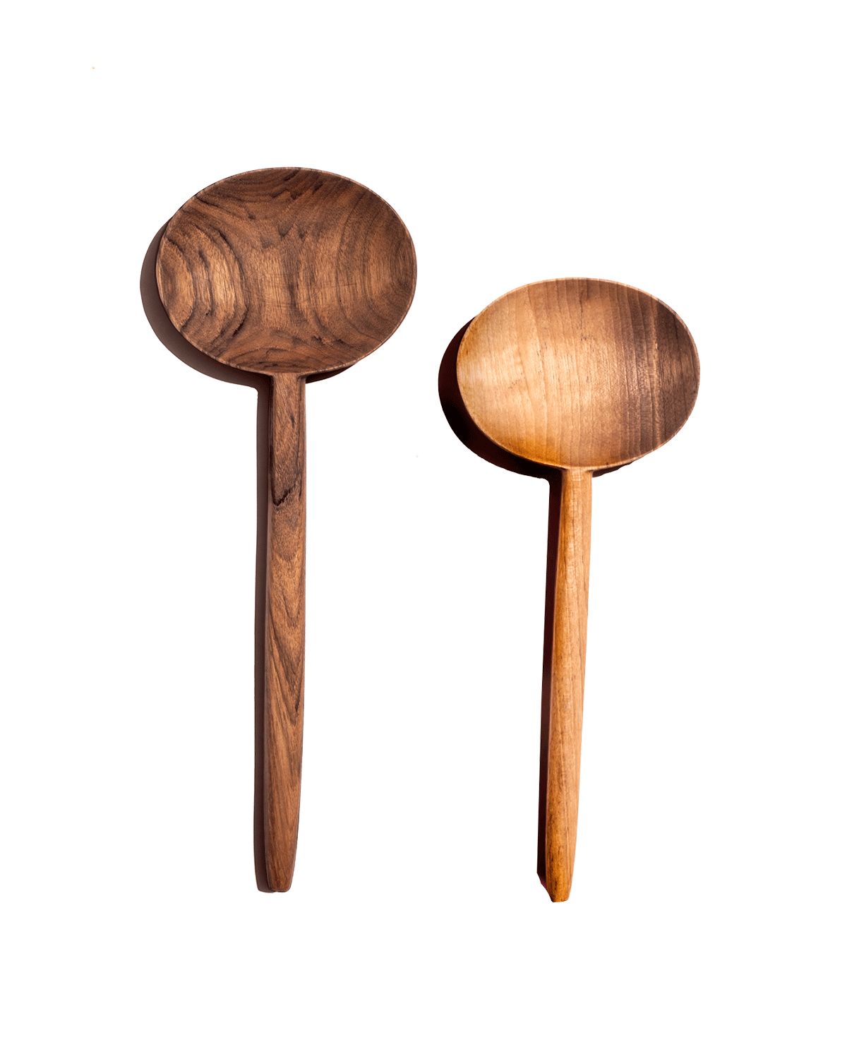 Two carved walnut oval serving spoons, one dark and one honey-toned, laid side by side on a green background