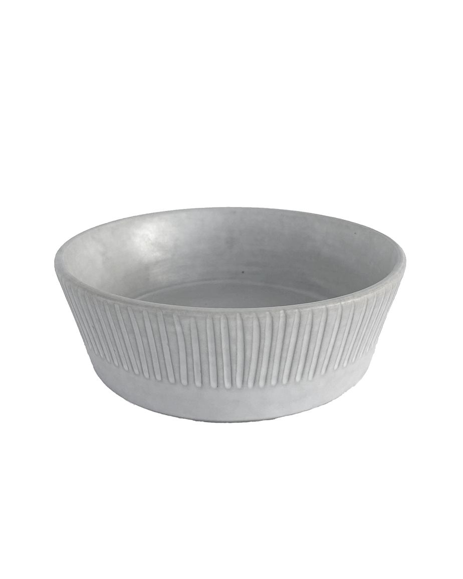 Carved matte white ceramic serving bowl with vertical lines around the outside on a black background